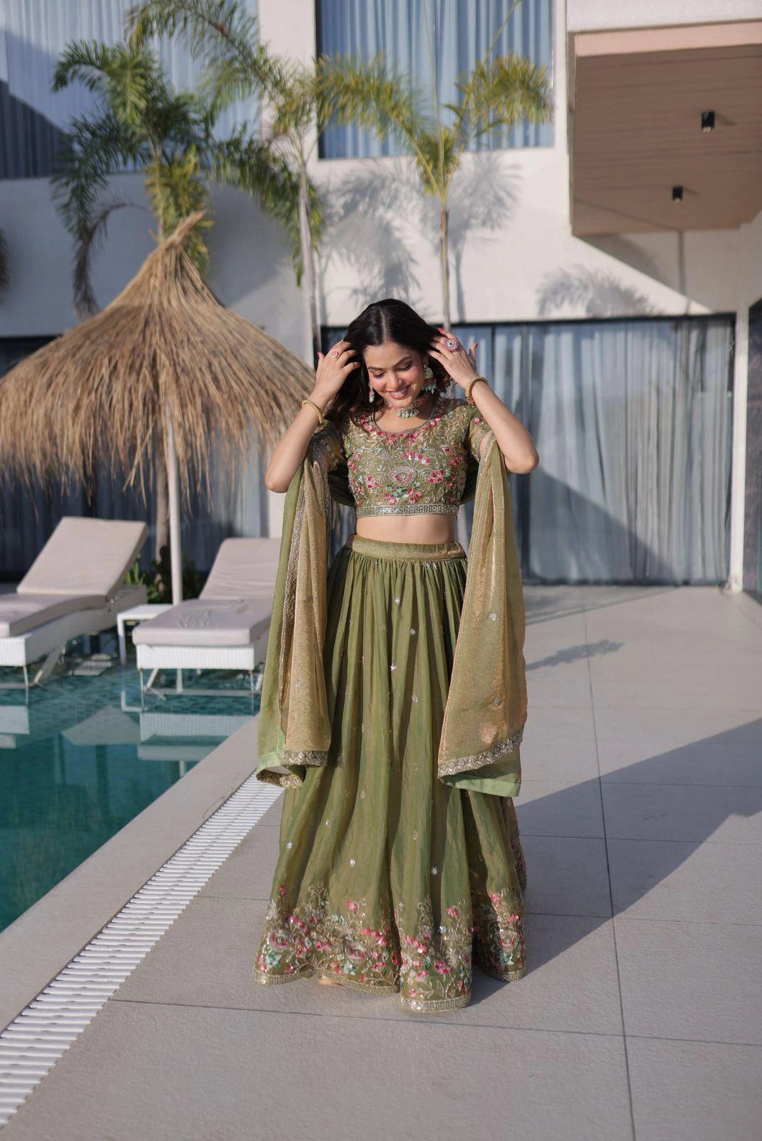 Woman in a green traditional outfit standing by a poolside.