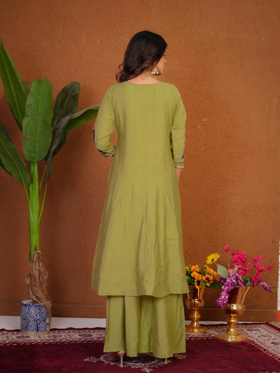 Woman in a green outfit standing in front of a brown wall with decorative elements.