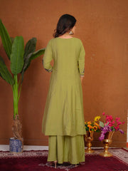 Woman in a green outfit standing in front of a brown wall with decorative elements.