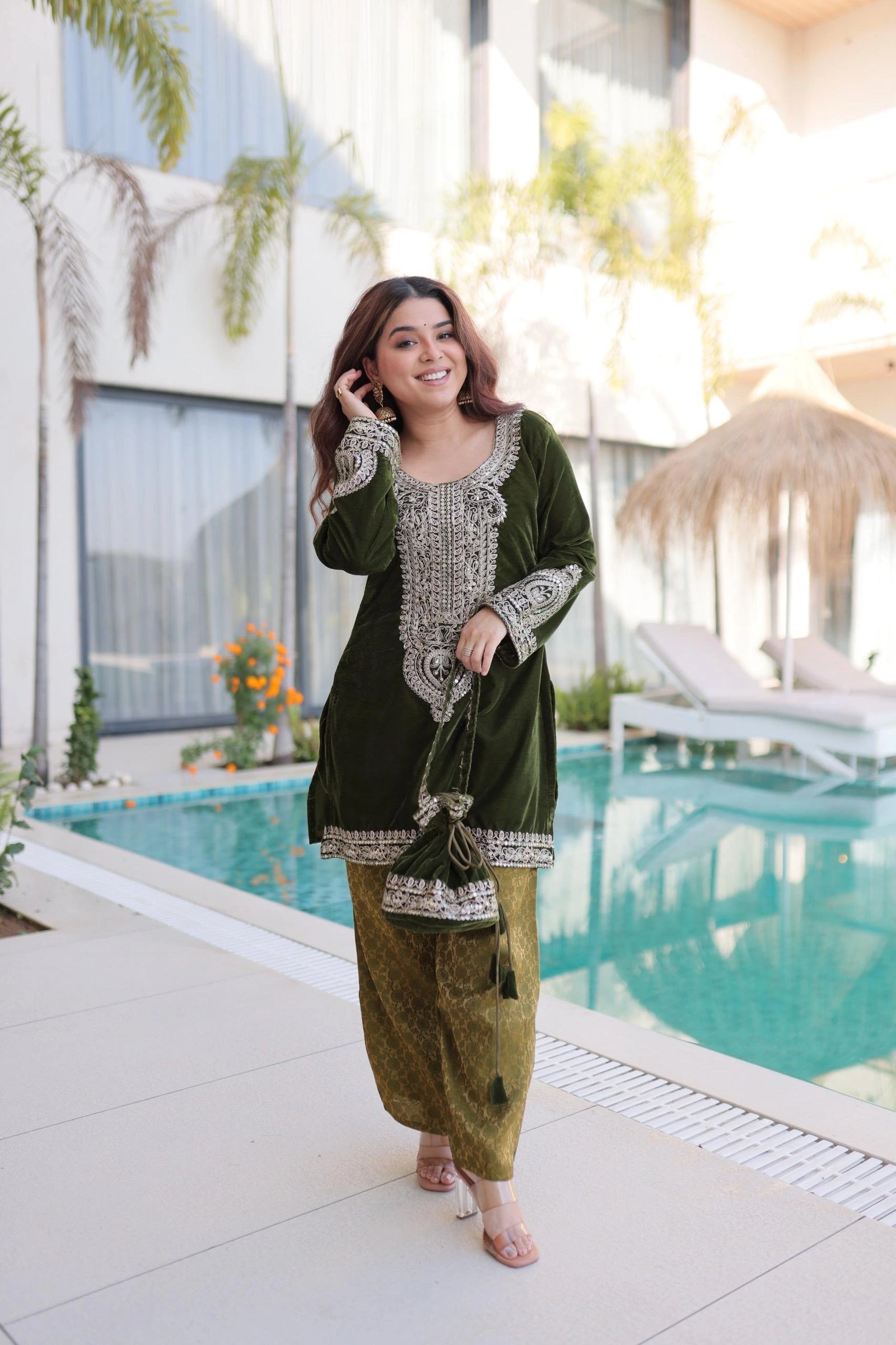 Woman in a green traditional outfit standing by a poolside.