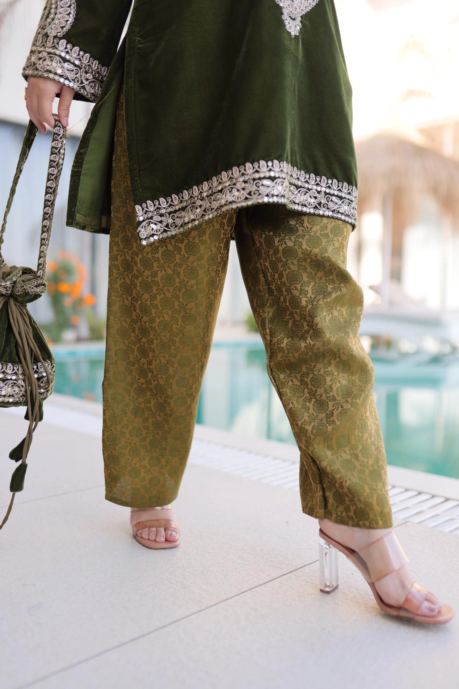Person wearing a green outfit with patterned pants and a matching top, holding a handbag.