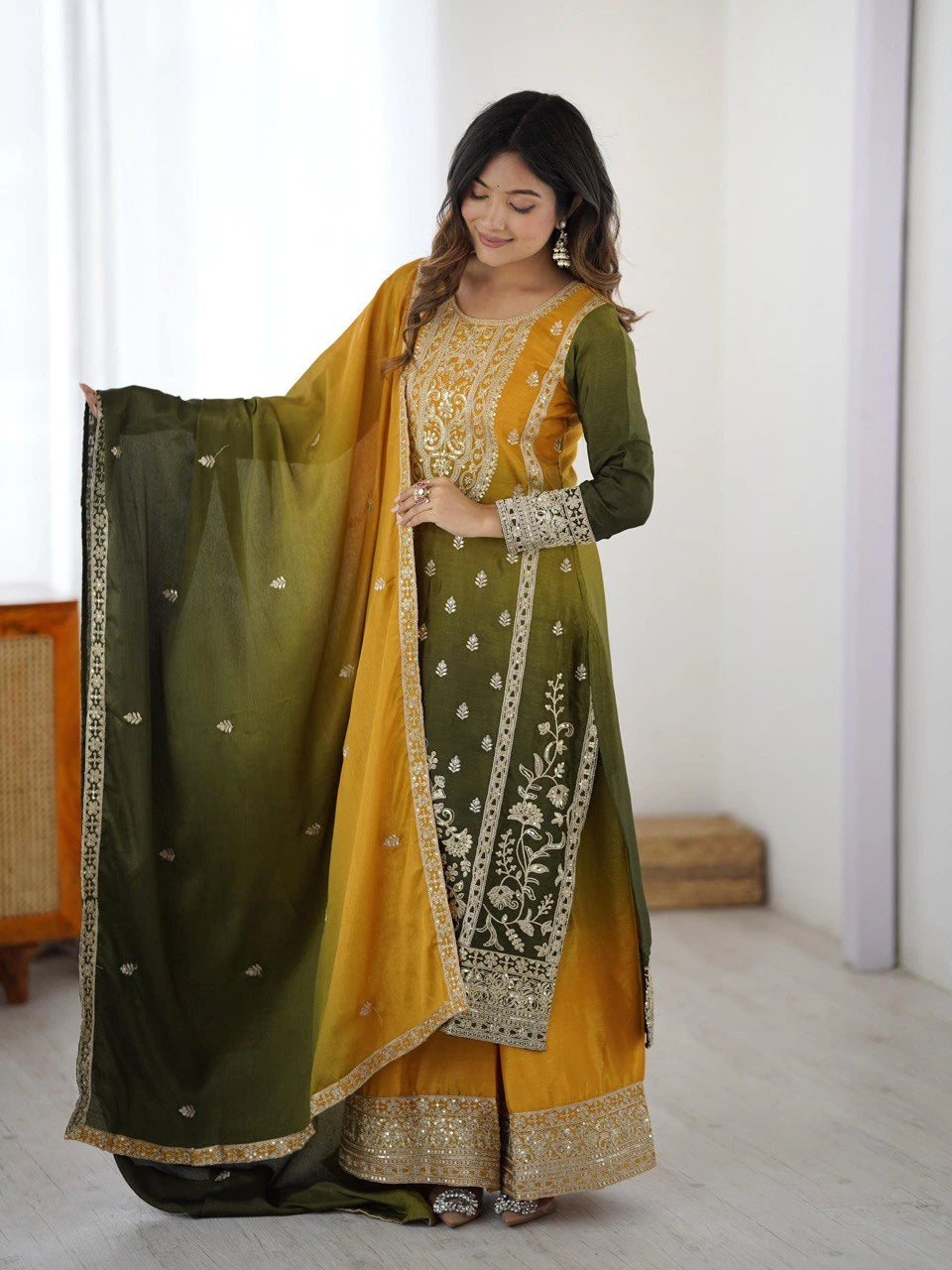 Woman wearing a green and yellow traditional outfit with embroidery in a minimal indoor setting.