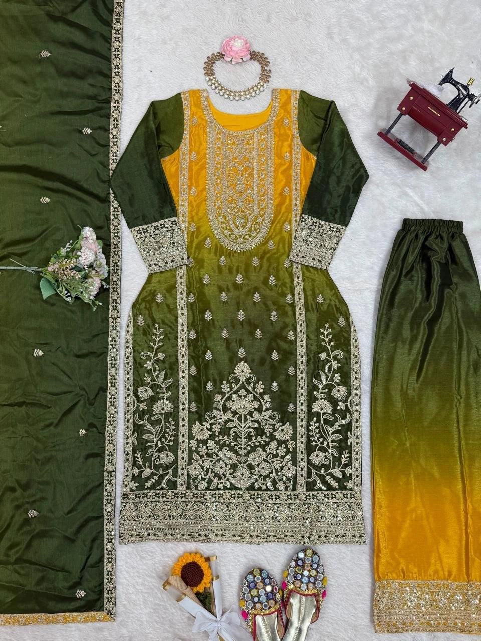 Green and yellow embroidered traditional outfit with jewelry and shoes on a light gray background
