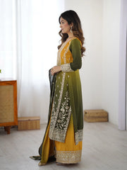 Woman wearing a green and yellow traditional outfit with embroidery in a minimal indoor setting.