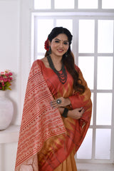 A woman models a graceful Copper Orange Soft Tussar Silk Saree. The saree features a zigzag pattern where the body meets the pallu, and the pallu has a wide panel of dense white and red geometric tribal-style print. She wears a coral blouse and a chunky dark beaded necklace, posing indoors by a large window.