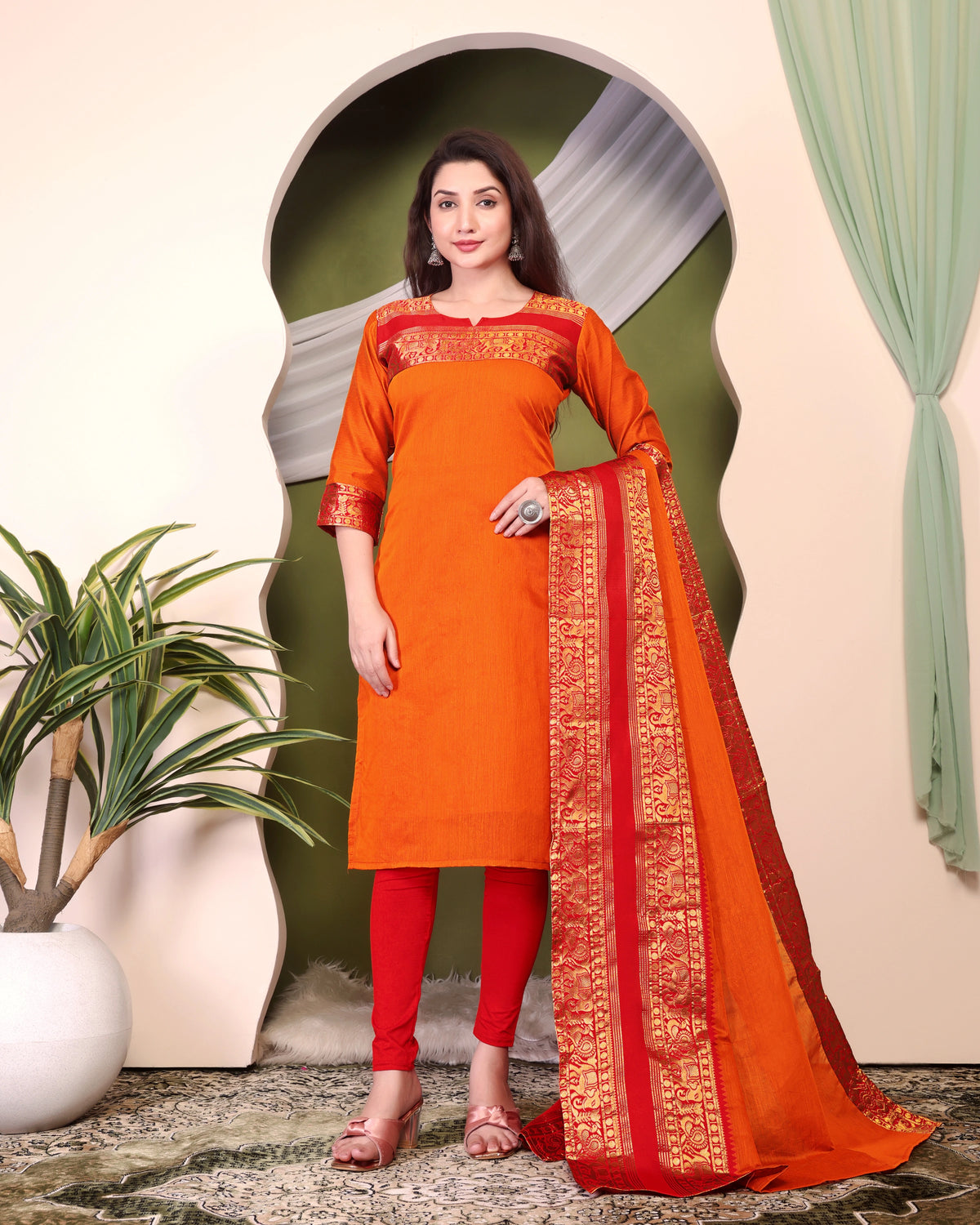 Woman wearing an orange and red traditional outfit with a matching dupatta in a decorative setting.