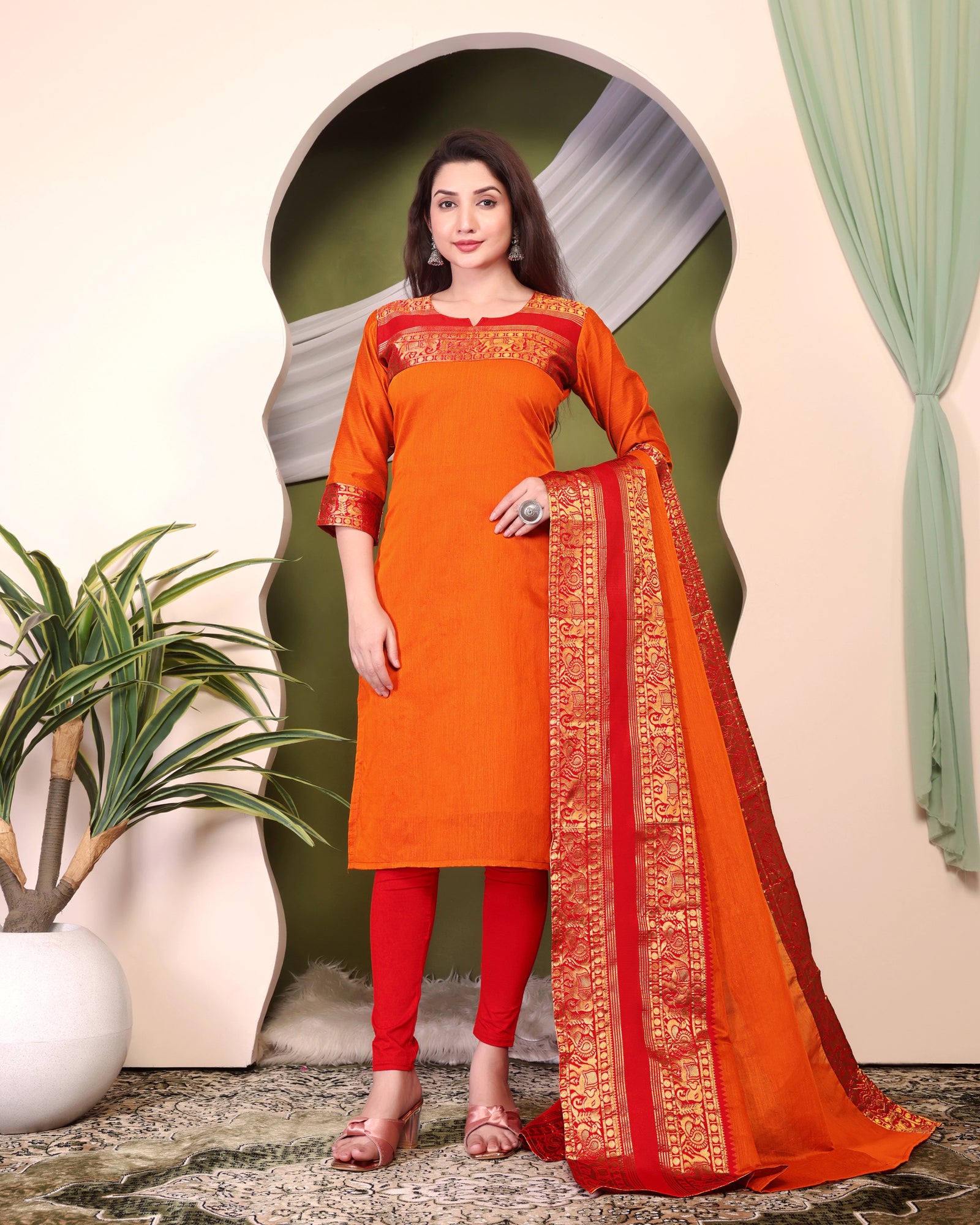 Woman wearing an orange and red traditional outfit with a matching dupatta in a decorative setting.