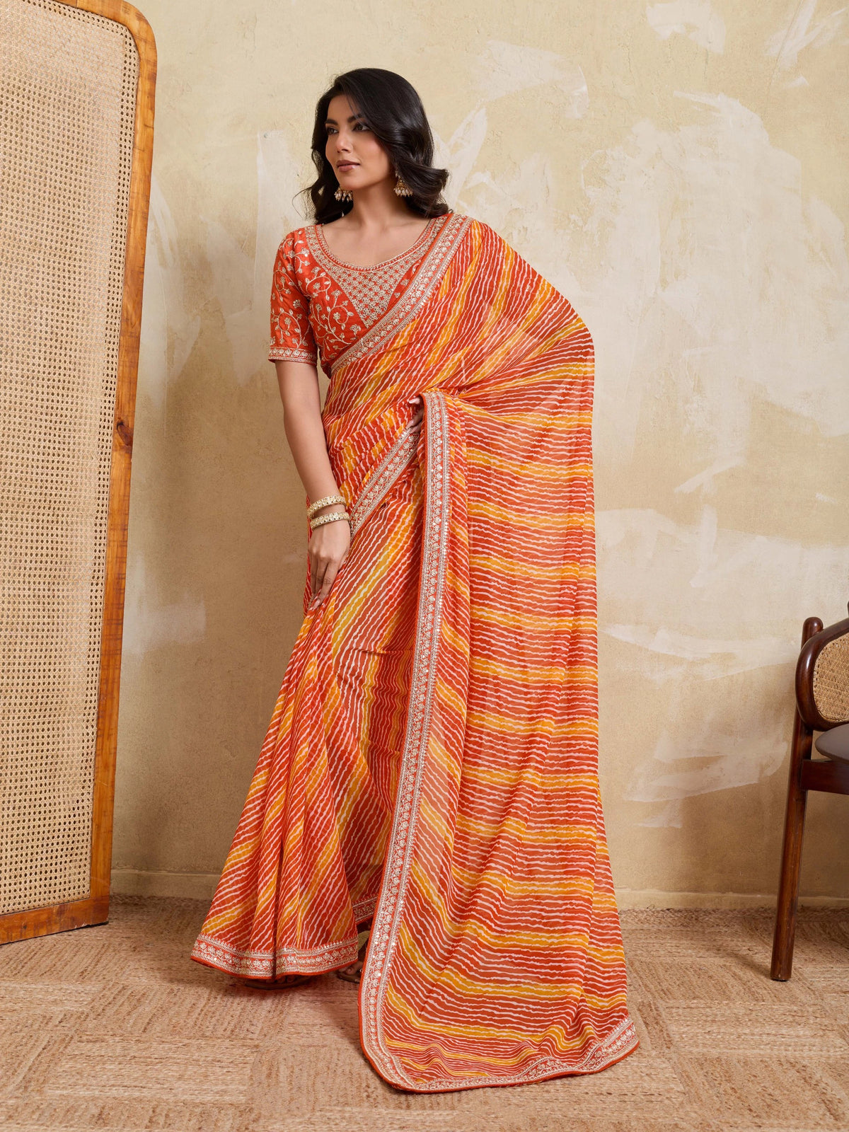 Woman wearing an orange and yellow saree with a textured wall background