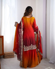 Woman wearing a red and orange traditional outfit with intricate designs in a bright room.