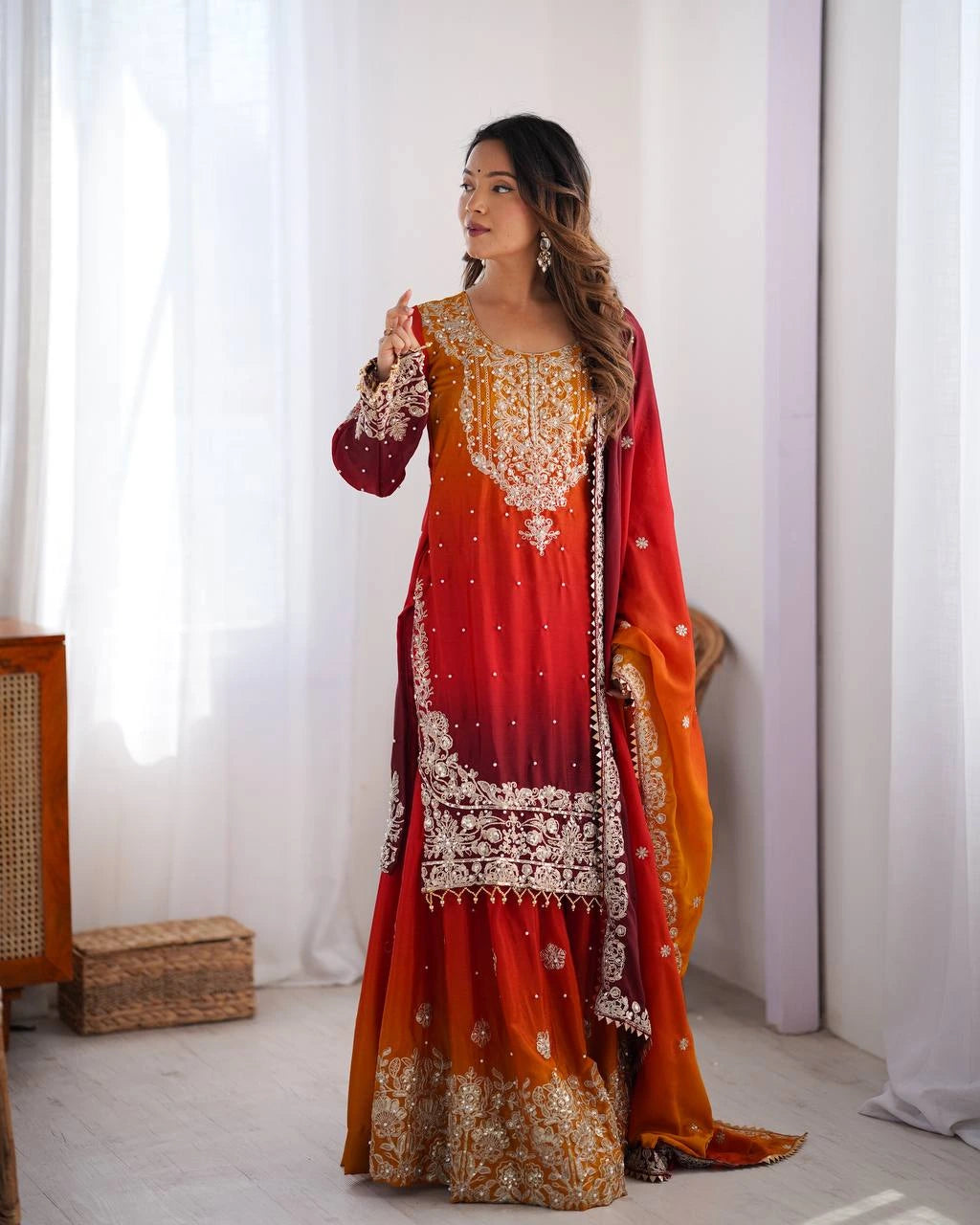 Woman wearing a red and orange traditional outfit with white embroidery in a bright room.