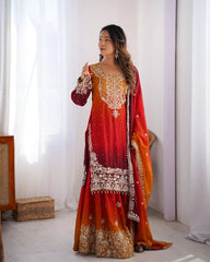 Woman wearing a red and orange traditional outfit with white embroidery in a bright room.