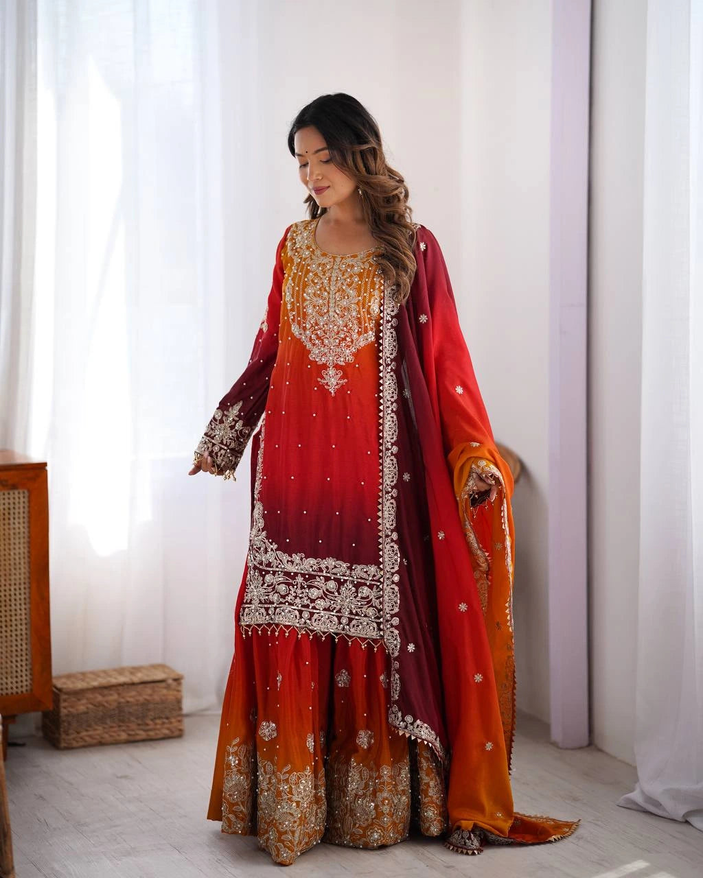 Woman wearing a traditional red and orange embroidered outfit in a bright room.