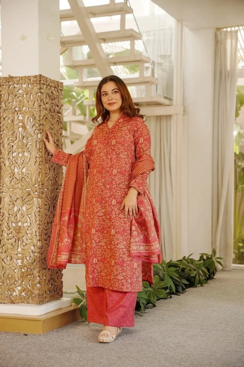 Woman in a red and pink traditional outfit standing next to an ornate column indoors.