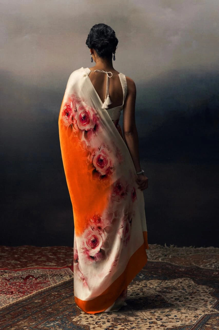 Woman holding a floral saree with an orange and white gradient.