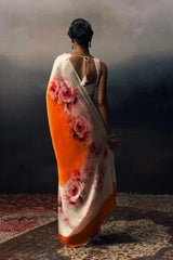 Woman holding a floral saree with an orange and white gradient.