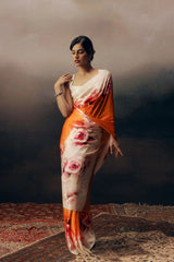 Woman wearing a floral saree with an orange border against a dark background