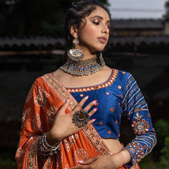 Woman in traditional orange and blue outfit with jewelry, blurred background