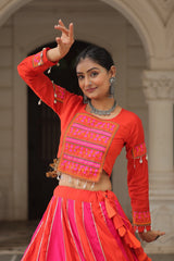 Woman in traditional red and pink outfit with intricate designs, standing in an archway.
