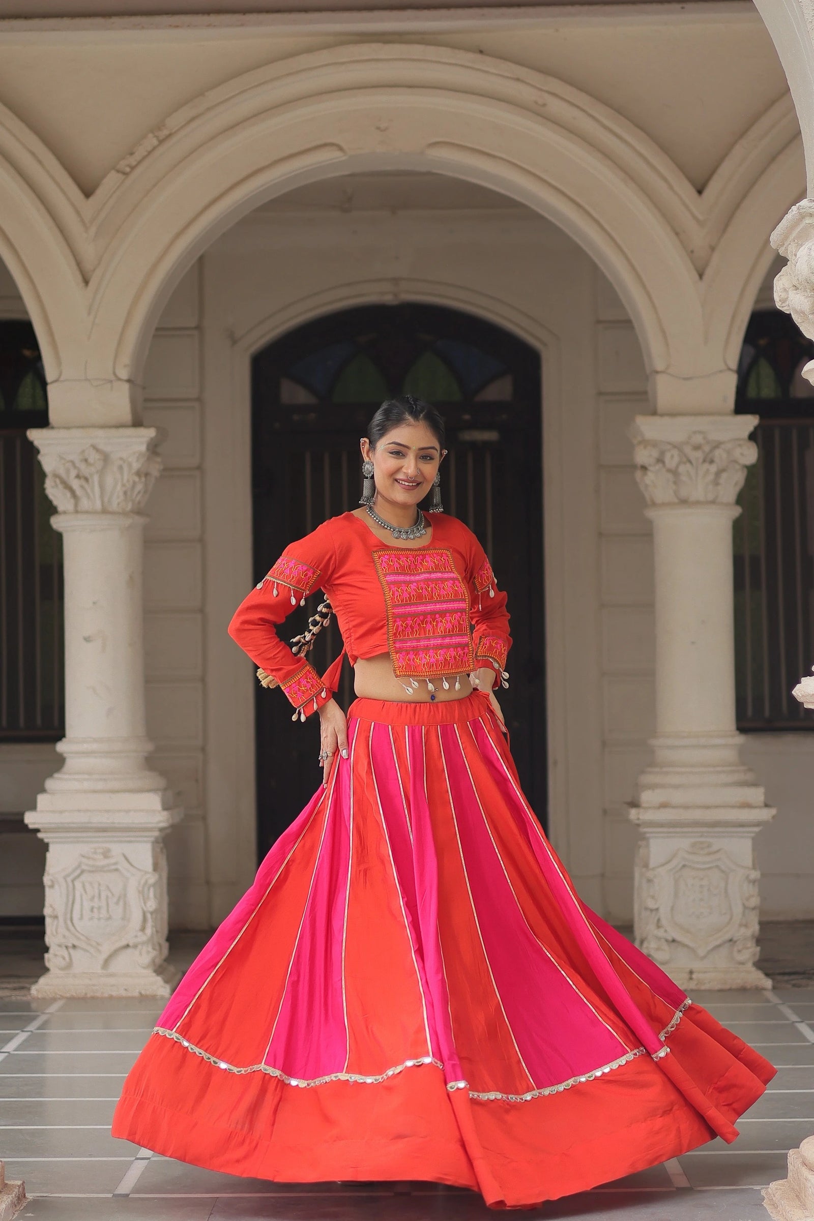 Woman in a traditional red and pink outfit standing in front of an archway.