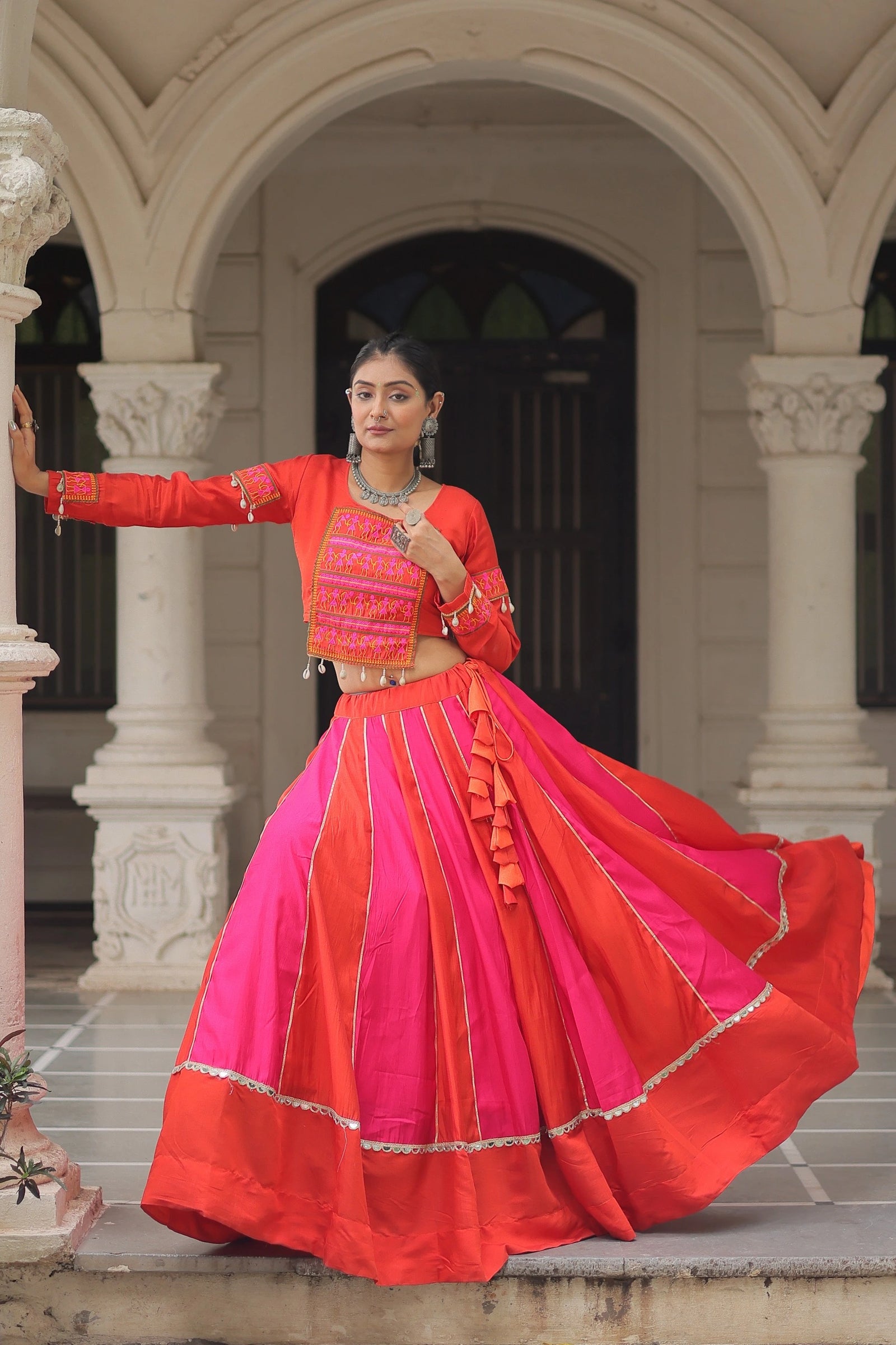 Woman in a vibrant red and pink traditional outfit standing in front of an archway.