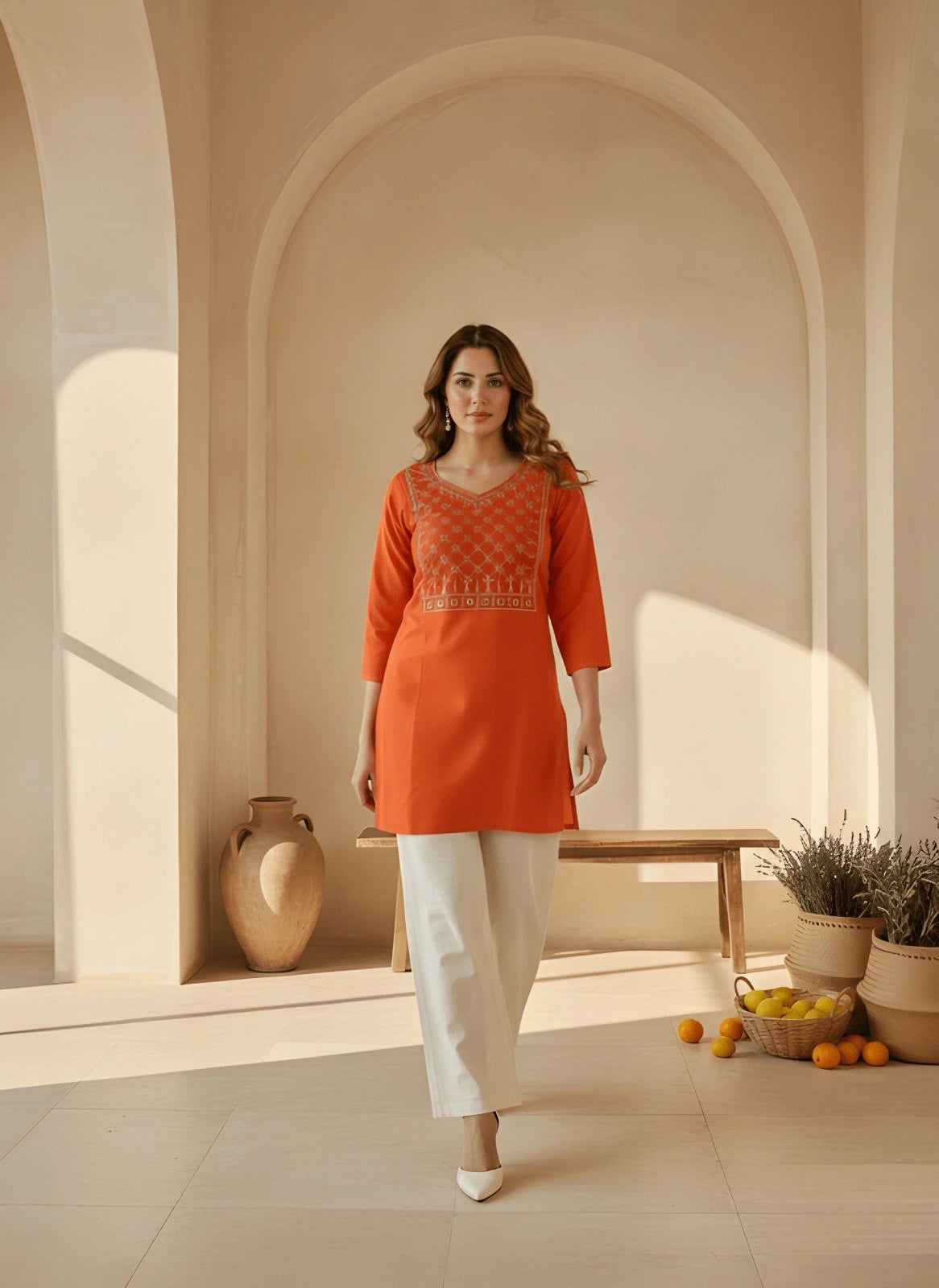 Woman in an orange dress standing in a sunlit room with arches and decorative elements.