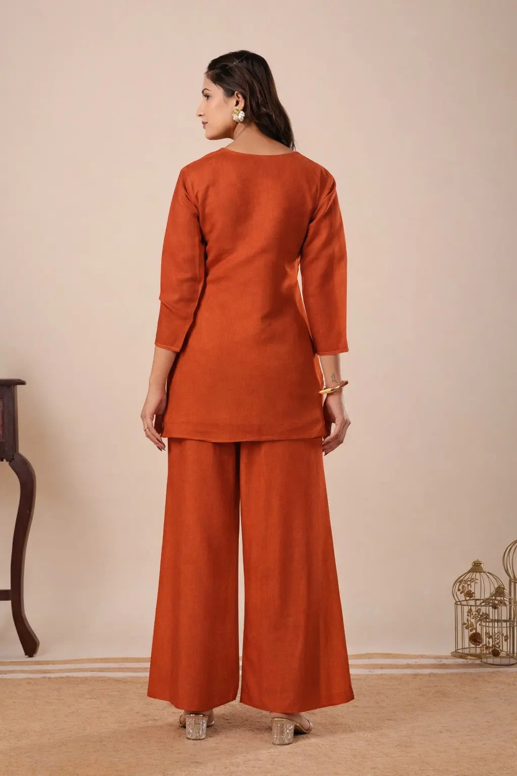 Woman wearing a rust-colored outfit with wide-leg pants against a beige background