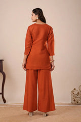 Woman wearing a rust-colored outfit with wide-leg pants against a beige background
