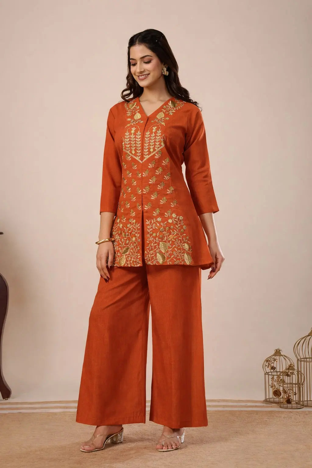 Woman wearing an orange traditional outfit with intricate patterns on a beige background