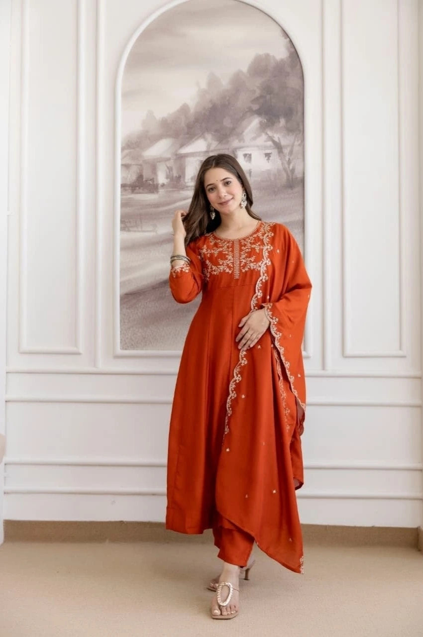 Woman wearing an orange embroidered dress standing in a room with white walls and a decorative mirror.