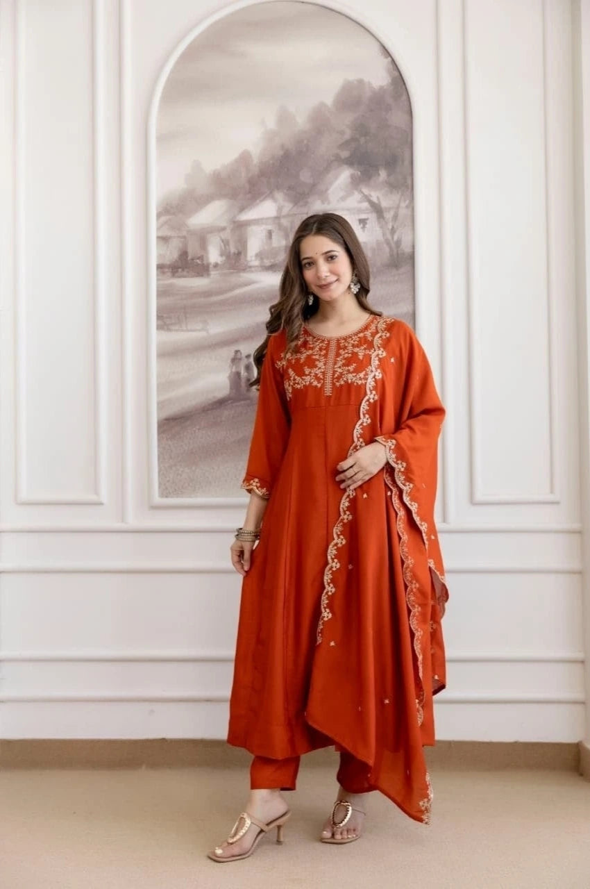 Woman wearing an orange traditional outfit with intricate embroidery in a decorative room.