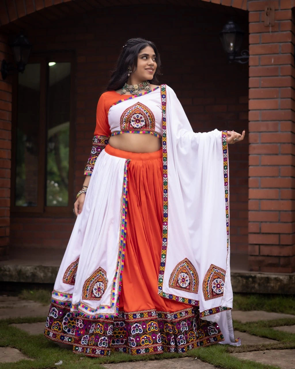 Woman in traditional orange and white outfit with colorful patterns standing outdoors.