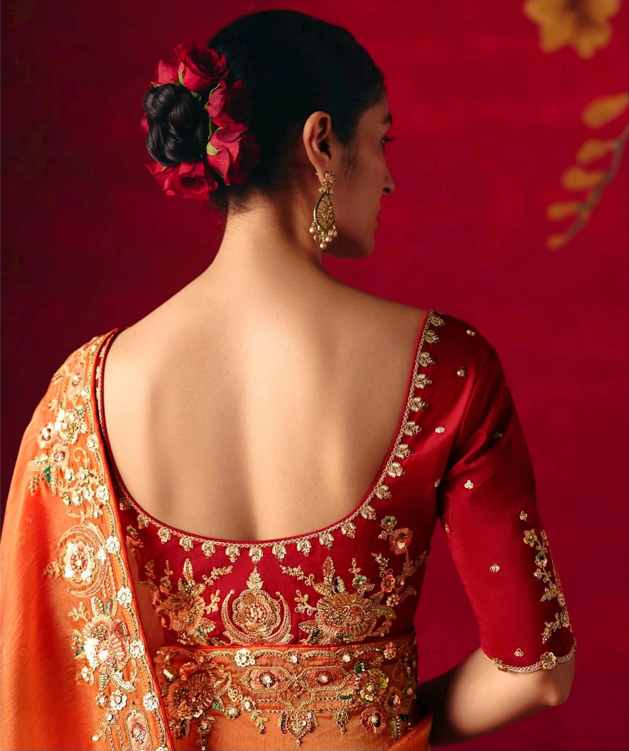 Woman wearing a traditional red and orange embroidered outfit with floral hair accessory on a red background
