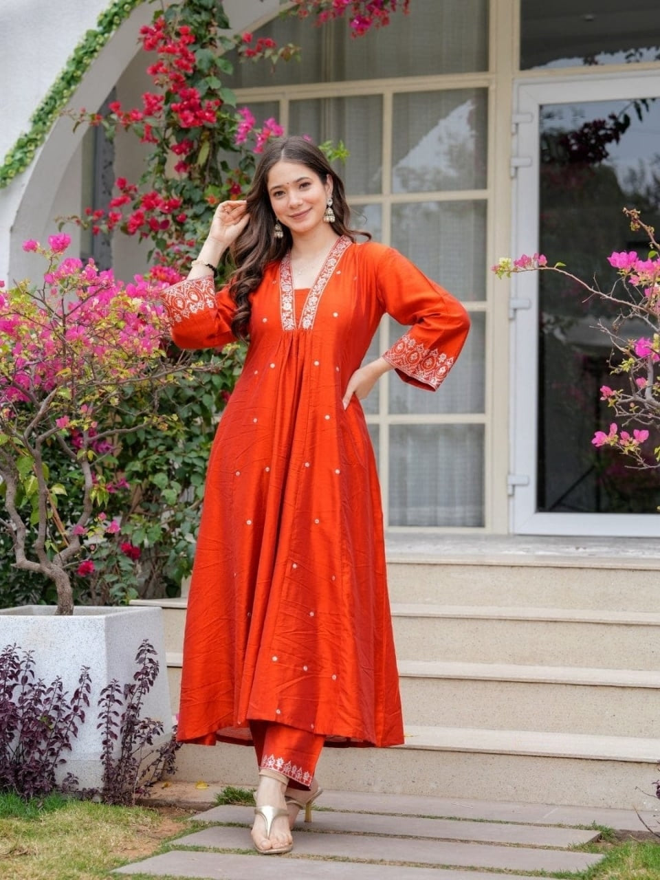 Woman in an orange dress standing outdoors with flowers and a building in the background