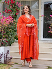 Woman in a red traditional outfit standing outdoors with flowers and a building in the background
