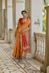 Woman in an orange and red saree standing in a decorative outdoor setting.