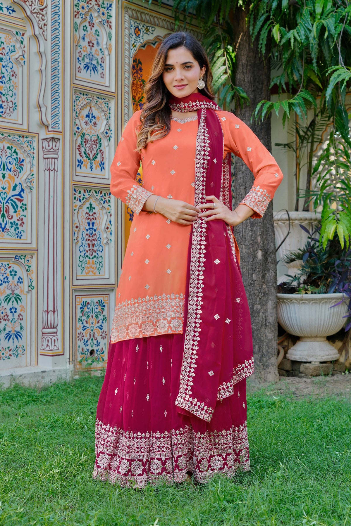 Woman in traditional pink and orange outfit with embroidered details standing in a garden.