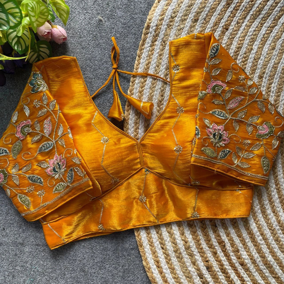 Mustard yellow embroidered blouse on a textured surface with a plant in the background