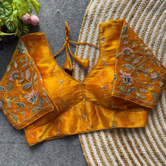 Mustard yellow embroidered blouse on a textured surface with a plant in the background