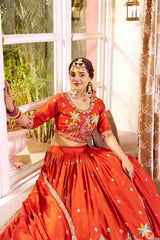 Woman in a traditional red outfit with floral patterns sitting by a window.