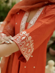Close-up of a red outfit with intricate white embroidery on a blurred natural background