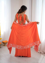 Woman wearing an orange traditional outfit with a sheer dupatta in a bright room.
