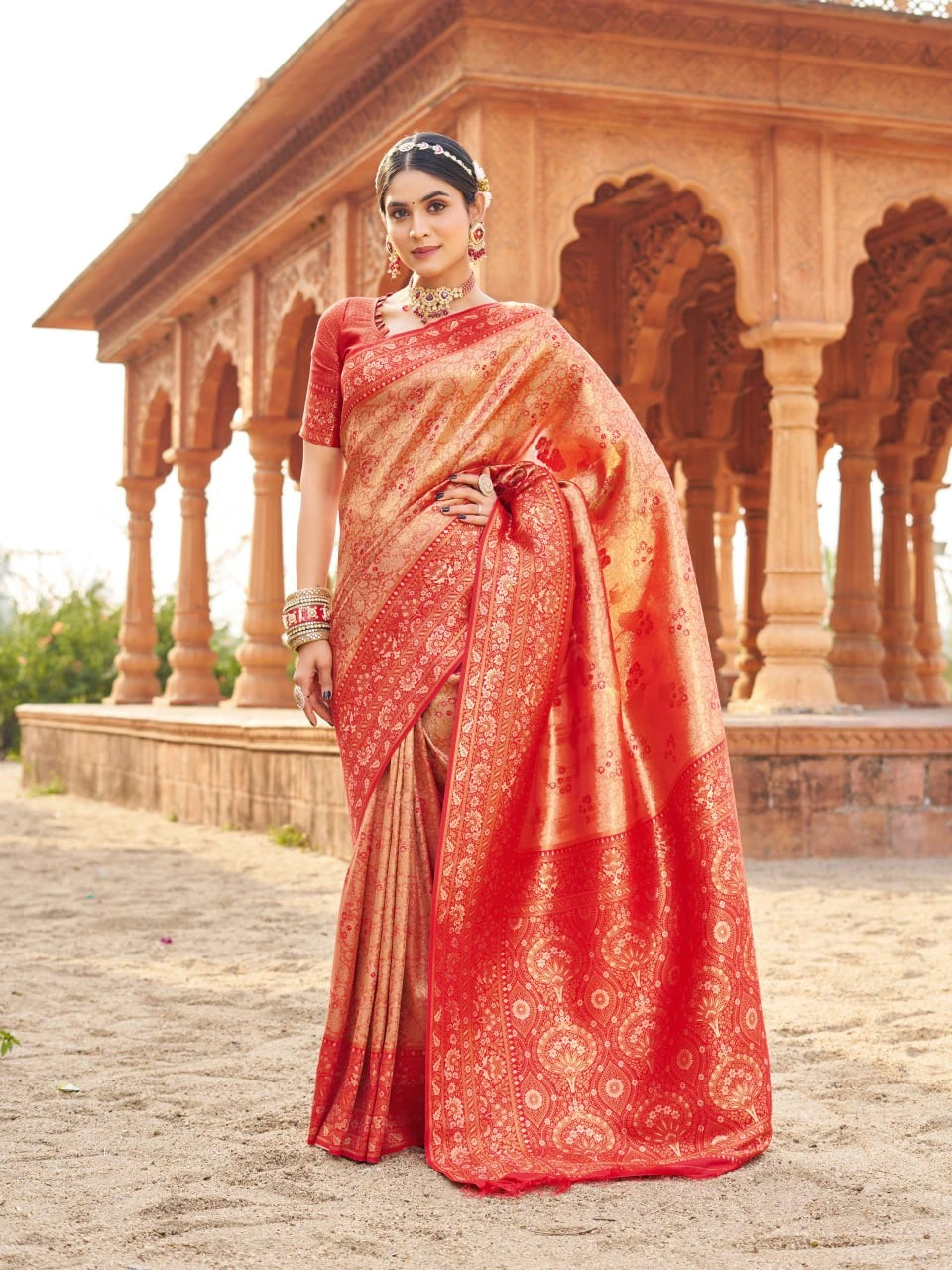 Woman in a red saree standing in front of an architectural structure.