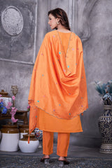 Woman wearing an orange traditional outfit with a shawl in a decorative setting.