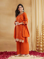 Woman wearing an orange traditional outfit with gold details against a beige background.