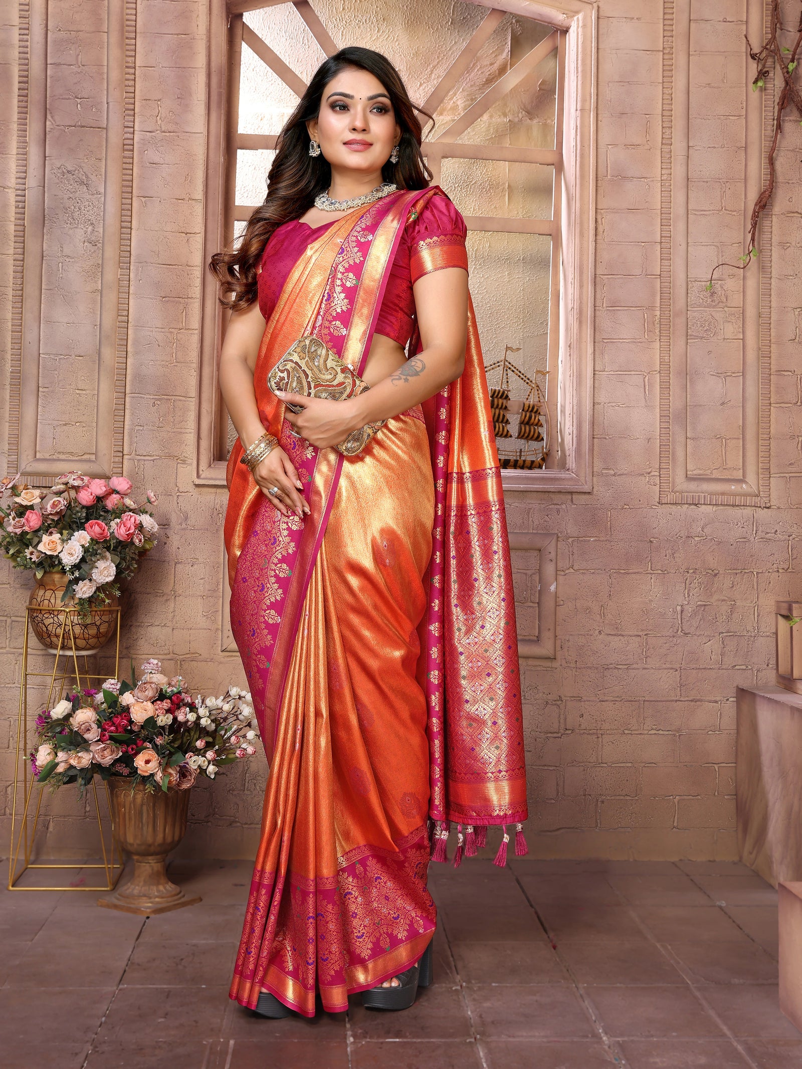 Woman wearing a traditional orange and pink saree with a brick wall background
