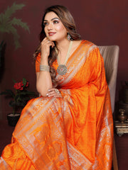 Woman in an orange saree with intricate patterns, sitting against a dark background.