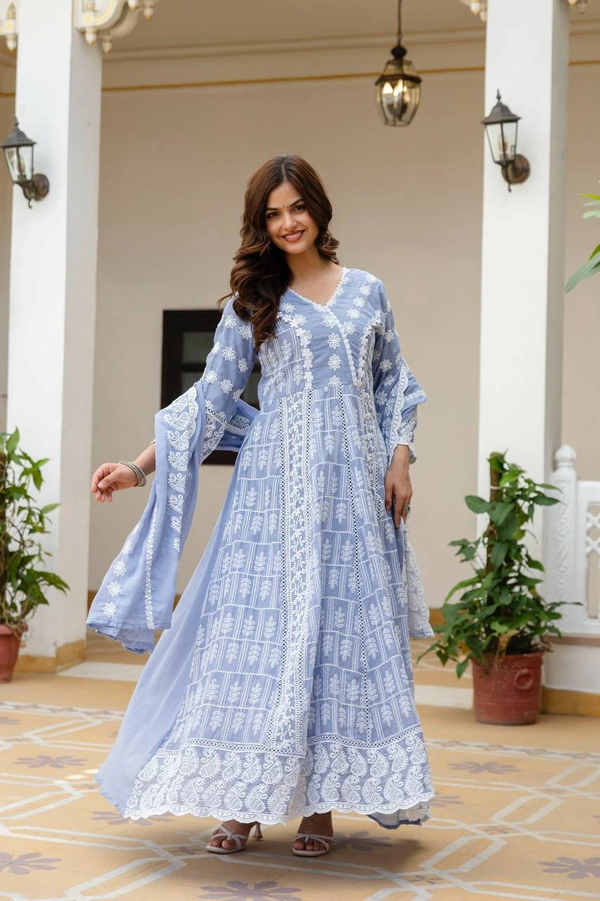 Woman in a blue patterned dress standing in an elegant indoor setting with columns and plants.