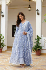 Woman in a light blue traditional outfit standing in an elegant indoor setting with plants and decorative lights.
