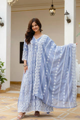 Woman wearing a light blue traditional outfit with white patterns in an indoor setting.