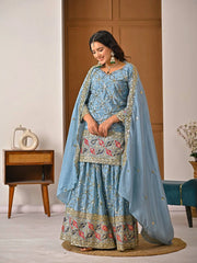 Woman in a traditional blue embroidered outfit with a matching dupatta in a room.